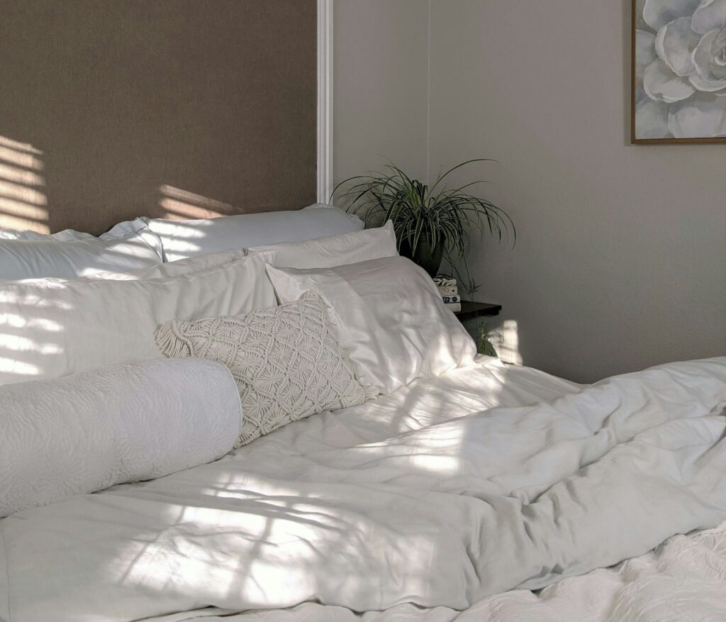 Lit aux draps blancs avec coussins et plante, lumière naturelle douce du matin